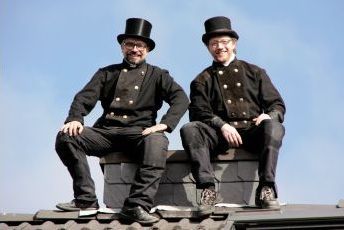 Arno Berger & Guido Rehm in Schornsteinfegermontur auf einem Dach sitzend